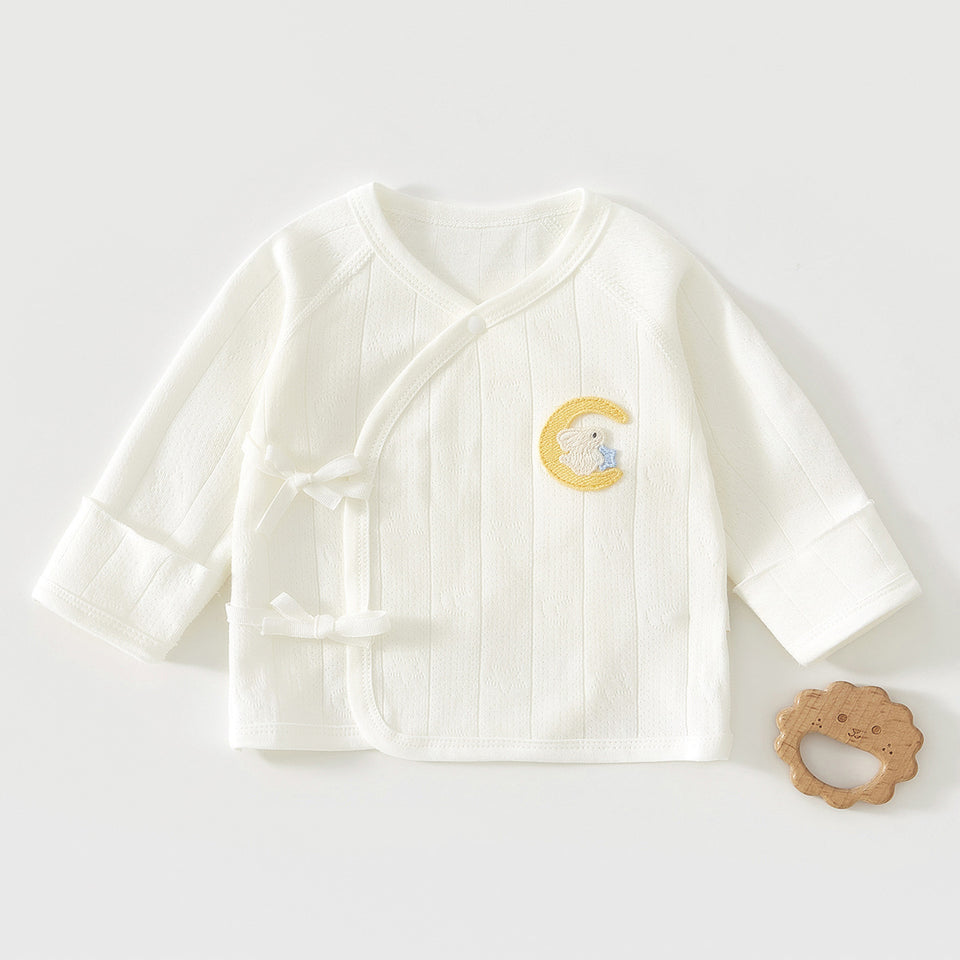 Weißes Wickelshirt mit Mond-Stickerei neben einem Holzspielzeug
