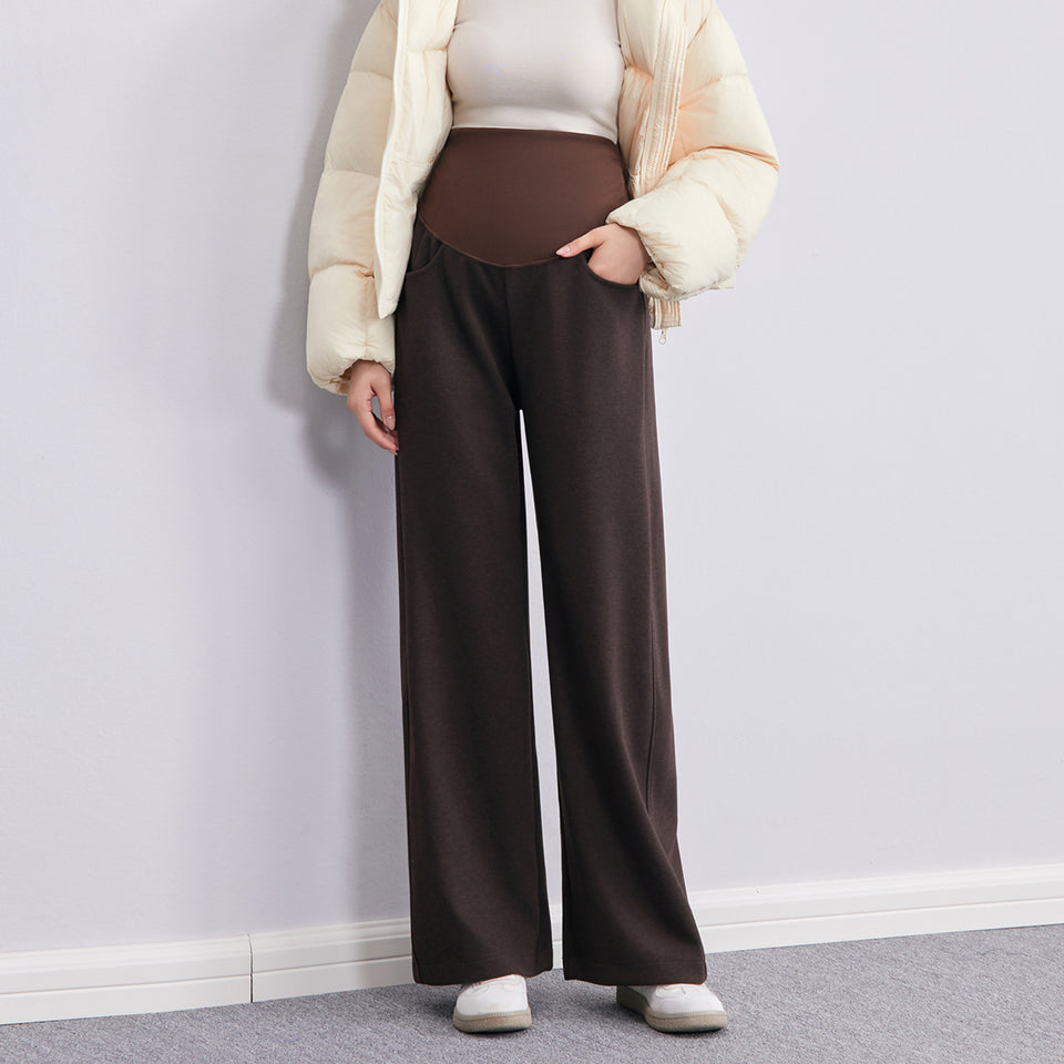 Frau in brauner weiter Umstandshose mit geradem Bein, dazu cremefarbene Daunenjacke