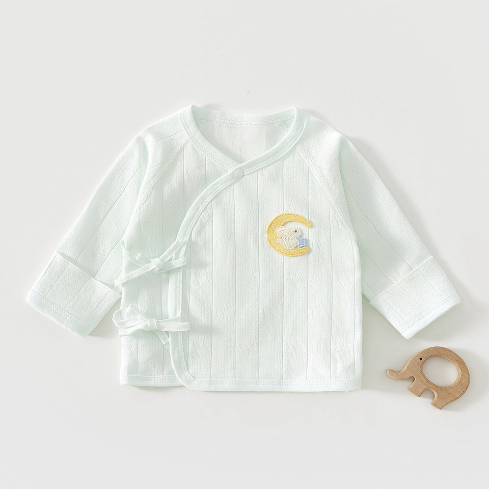 Mintfarbenes Wickelshirt mit Mond-Stickerei neben einem Holzspielzeug