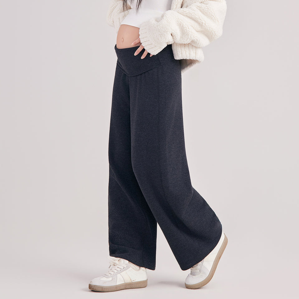 Frau in dunkler weiter Umstandshose mit Umschlagbund, dazu Pullover und Sneaker