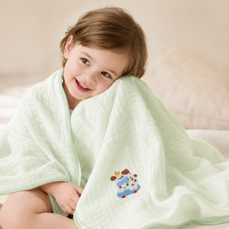 Kind in mintfarbenes Musselin-Badetuch mit Stickerei eingewickelt