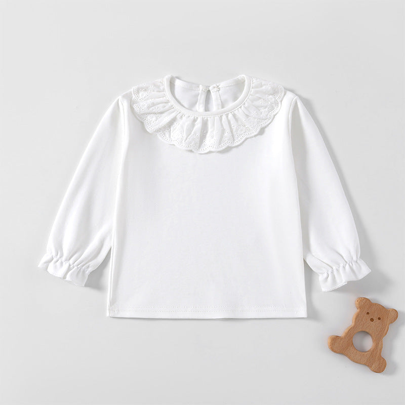 Weißes Langarmshirt mit Spitzenkragen und Volantärmeln neben einem Holzspielzeug