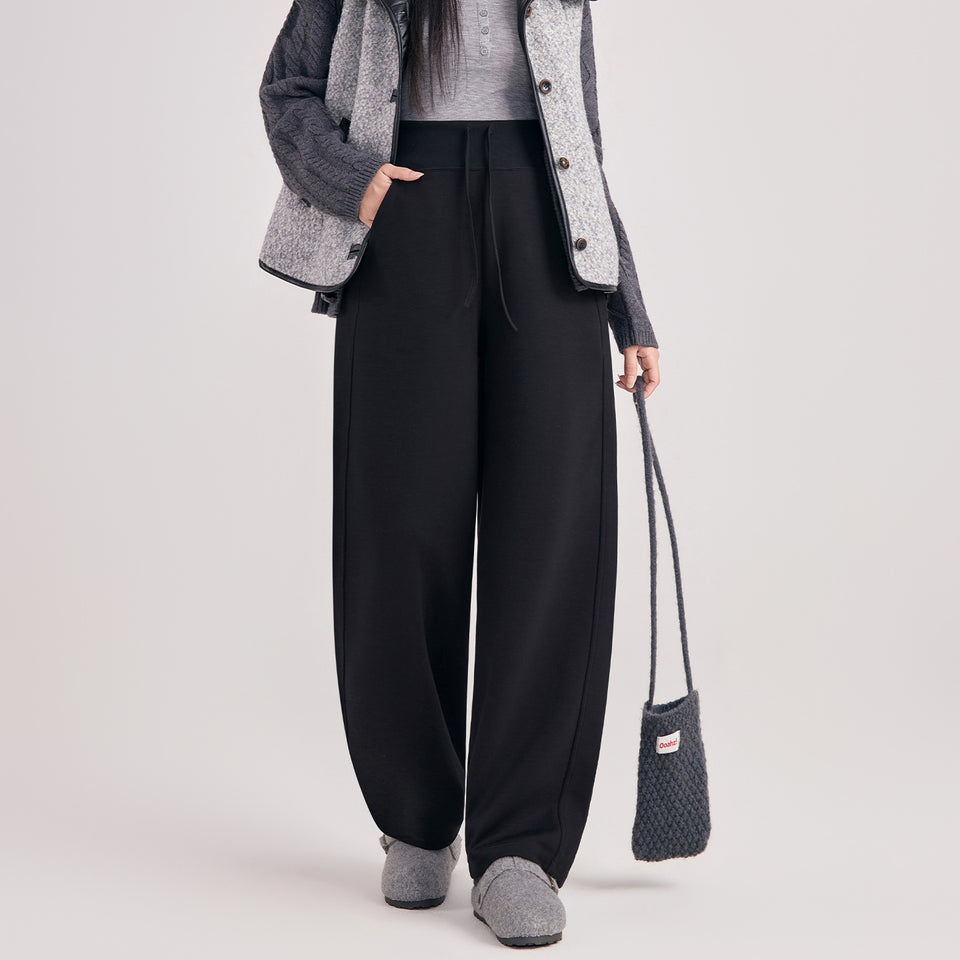 Frau in schwarzer weiter Umstandshose mit breitem Bund und Kordel, dazu Strickjacke und Tasche