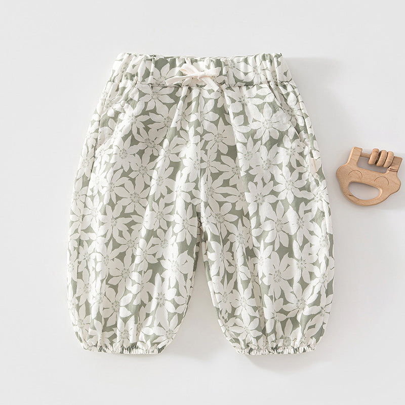 Grüne Baby-Sommerhose mit weißem Blütenmuster neben einem Holzspielzeug