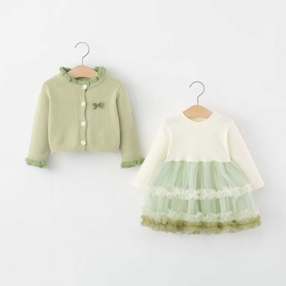 Grüne Strickjacke und cremefarbenes Tüllkleid nebeneinander am Kleiderbügel