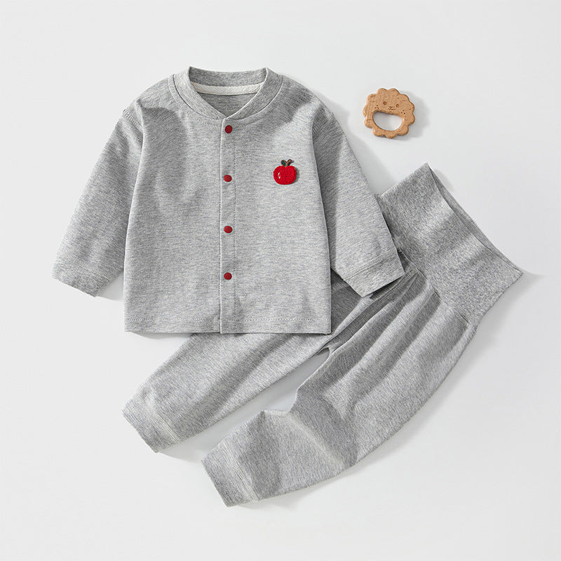 Graues Baby-Set mit roter Apfel-Applikation neben einem Holzspielzeug