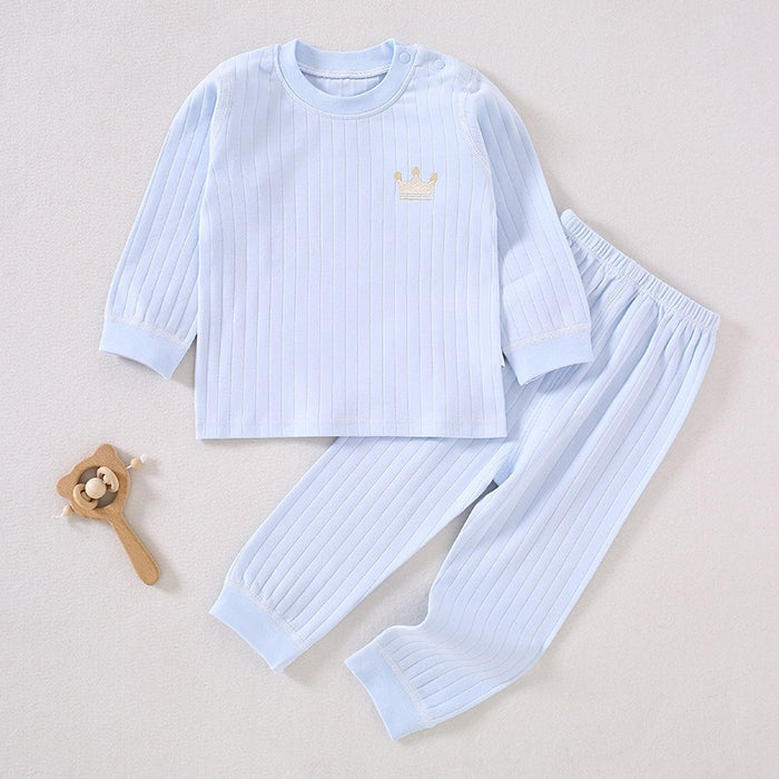 Hellblaues Baby-Set aus gerippter Baumwolle mit Krönchen-Stickerei neben einem Holzspielzeug