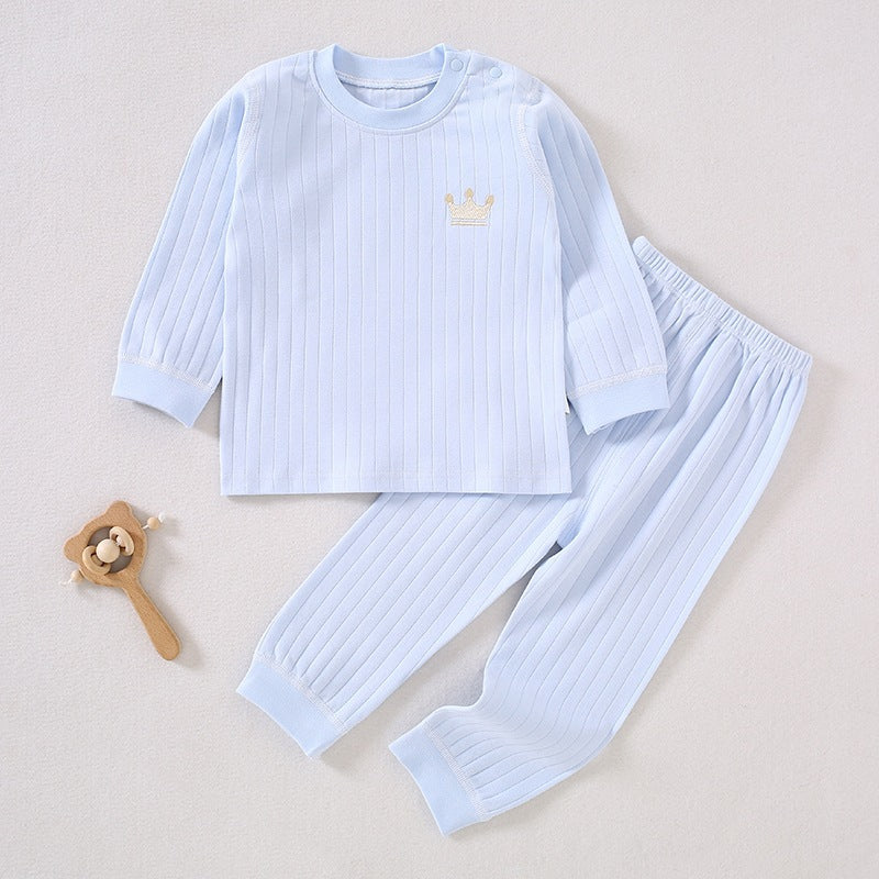 Hellblaues Baby-Set aus gerippter Baumwolle mit Krönchen-Stickerei neben einem Holzspielzeug