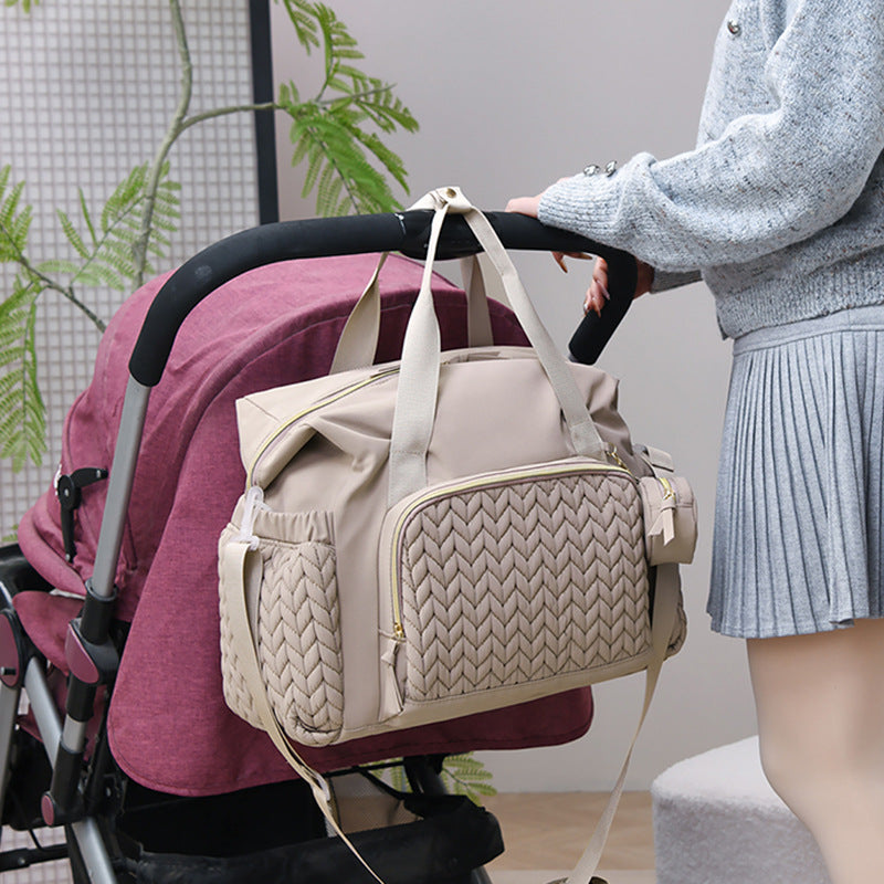 Beigefarbene Wickeltasche am Griff eines Kinderwagens eingehängt