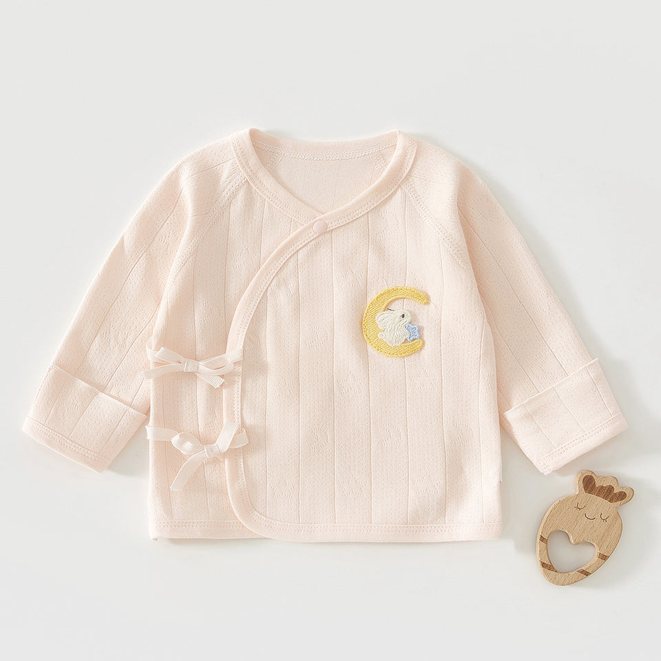 Rosa Wickelshirt mit Mond-Stickerei neben einem Holzspielzeug