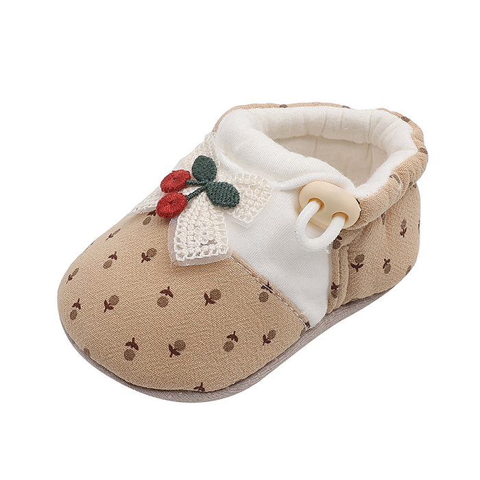 Ein khakifarbener Babyschuh mit Pünktchenmuster, Netzschleife und roter Kirsche auf weißem Hintergrund