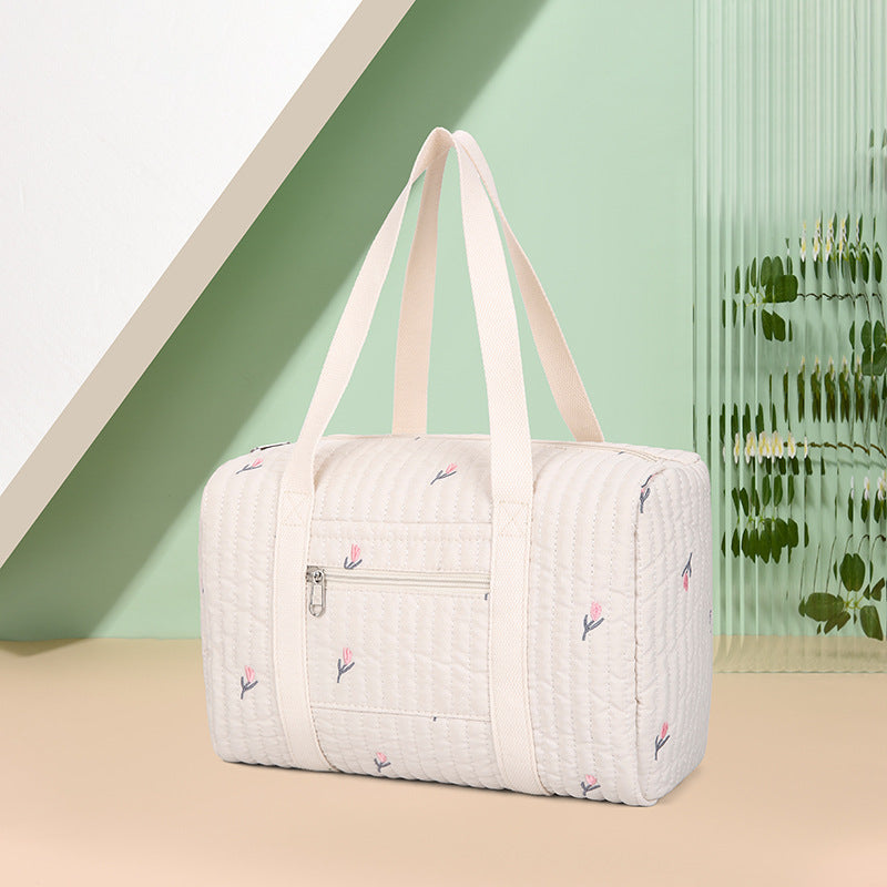 Cremefarbene gesteppte Tasche mit Tulpenstickerei vor pastellfarbenem Hintergrund