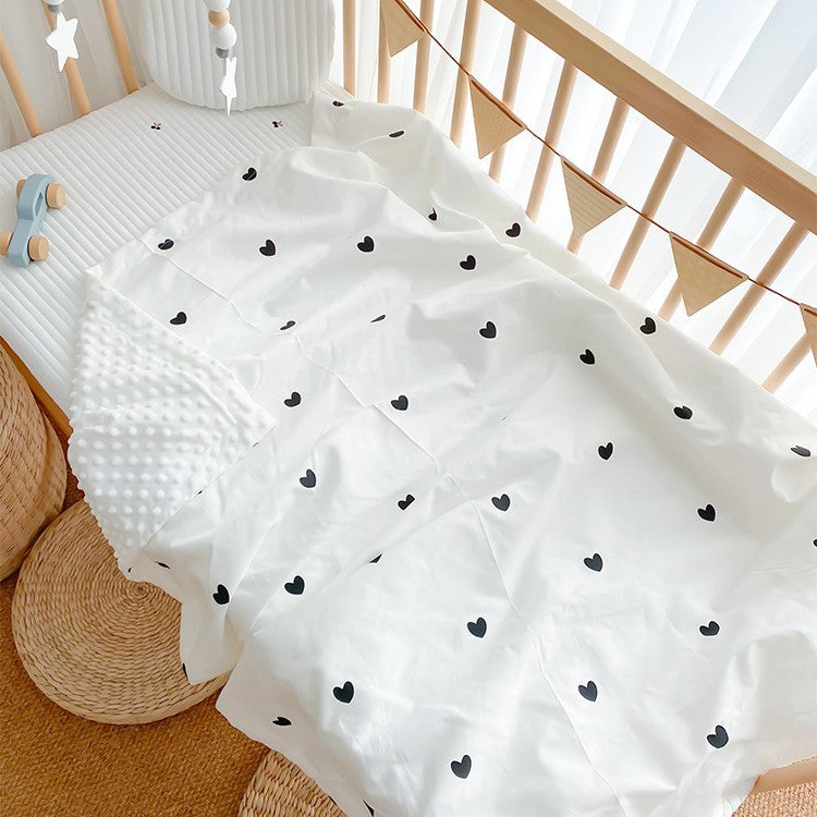 Babydecke mit kleinen schwarzen Herzen auf weißem Grund, im Babybett liegend