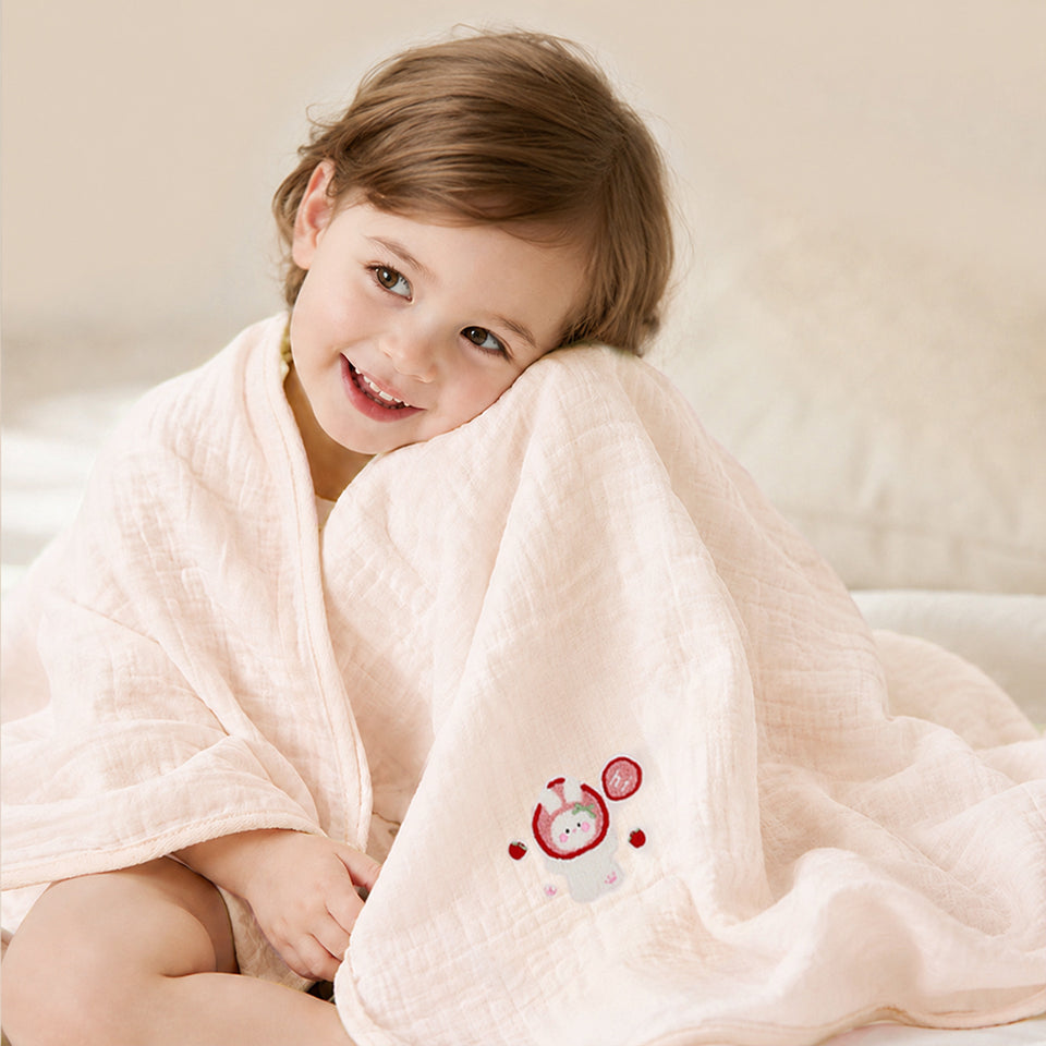 Kind in rosa Musselin-Badetuch mit Hasen-Stickerei eingewickelt