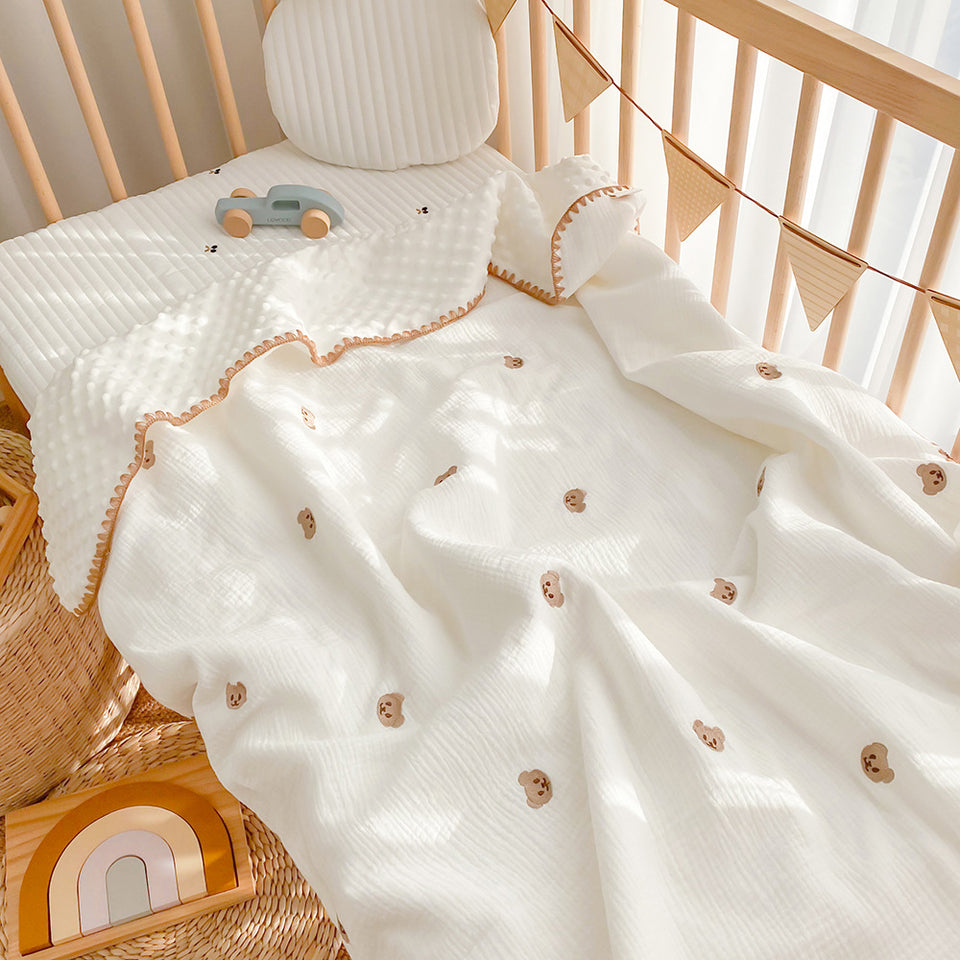Weiße Babydecke mit gesticktem Bären im Babybett